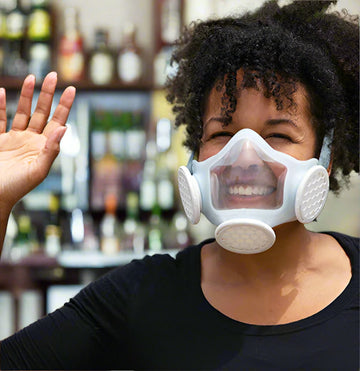 Young black woman wearing OmniMask and smiling and waving at friend.